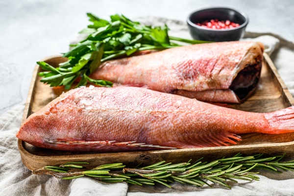 raw red sea perch in a wooden bowl with parsley gray background top view - Запечённый красный окунь