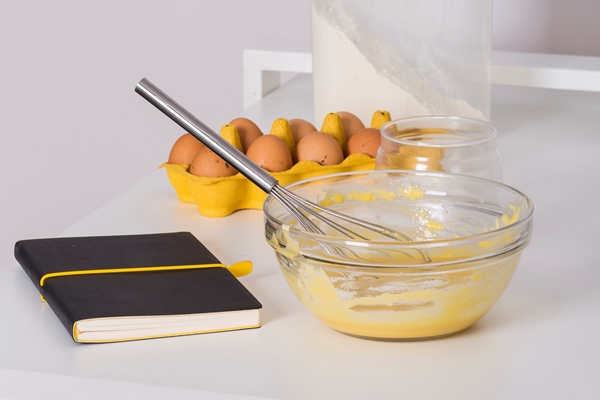 recipe book egg carton flour and whipped eggs on white table against white wall - Куличи александрийские