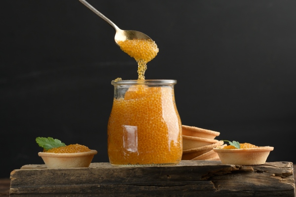 salted pike caviar in a glass jar on a wooden board close up - Оладьи из икры с луком и морковью