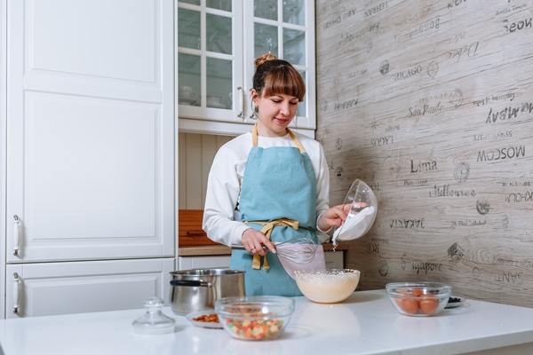 the woman cook adds flour to the dough the process of mixing cake ingredients in the home kitchen - Куличи александрийские