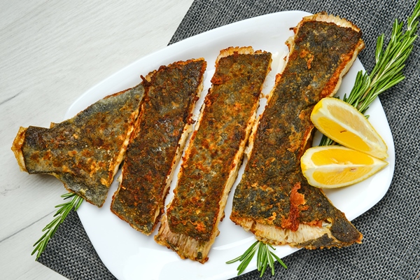 top view of fried flounder in breading cut on pieces served with lemon on white wooden table - Камбала жареная
