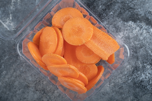 top view of plastic container full with carrot slices over grey background - Корюшка маринованная