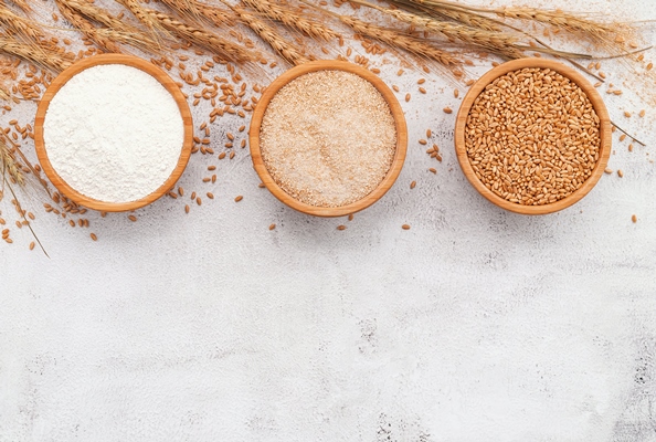 wheat grains brown wheat flour and white wheat flour in wooden bowl set up on white concrete background - Цукини, фаршированные кашей и баклажанами