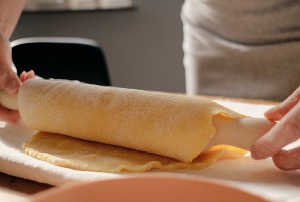 woman rolls out the dough with a rolling pin in the sun rays - Итальянская пасхальная пицца