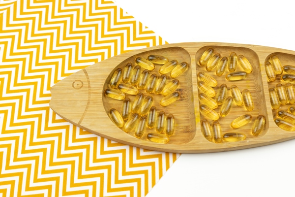 yellow capsules of omega 3 lie on a wooden plate in the form of the fish - Особенности питания детей