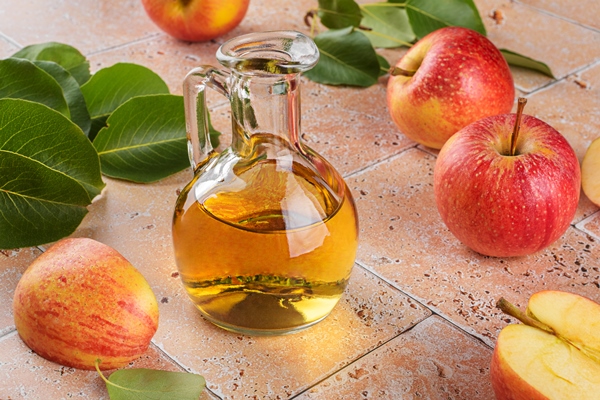 apple cider vinegar of fermented fruit in glass bottle with apples on beige travertine tiles table background - Маринованные бутоны черемши