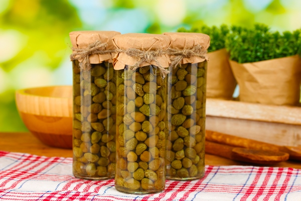 glass jars with tinned capers on green background - Маринованные бутоны черемши