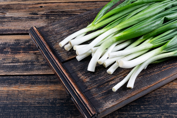 green spring onions or scallions on a cutting board on a dark wooden table - Салат из одуванчиков с огурцами и морковью