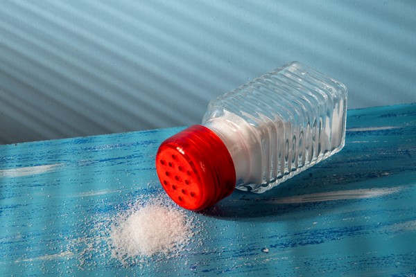 overturned salt shaker with salt on the side representing excess consumption - Сырная паста со снытью