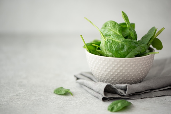 small leaves of fresh spinach in a gray bowl on a white table - Правила обработки и приготовления дикорастущих растений