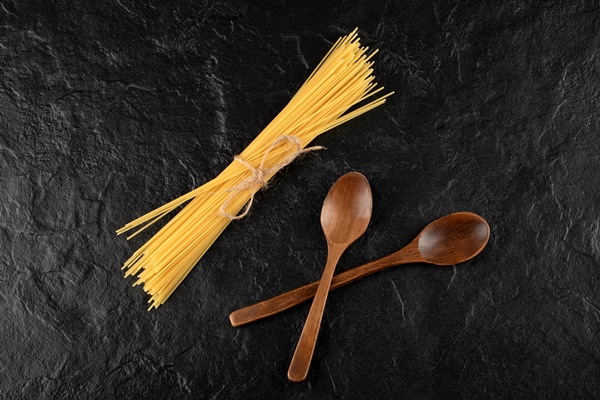 raw spaghetti and wooden spoons on black surface - Весёлые сосиски