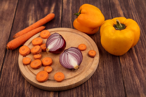 top view of fresh vegetables such as chopped carrots and red onions on a wooden kitchen board with carrots and yellow bell peppers isolated on a wooden background - Рыбные шашлыки с постным яблочным соусом