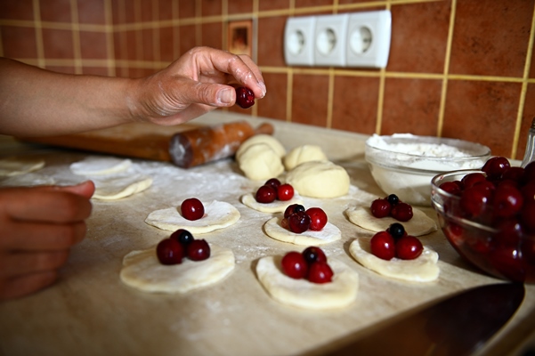 close up of female hands putting cherry berries on a round shape of dough filling ukrainian traditional dumplings process of cooking dumplings step by step in the kitchen - Вареники с вишней
