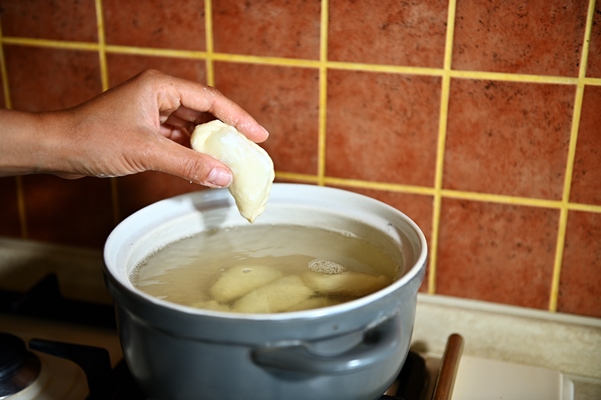 close up shot of female hand of pastry chef dipping cherry dumplings into a pot of boiling water process of cooking dumplings step by step food background - Вареники с вишней