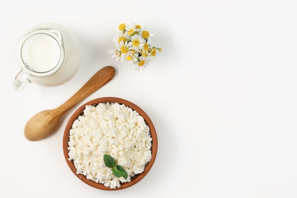 granulated cottage cheese in an earthen bowl next to wooden spoon and jug of milk layout on bright white background with copy space soft cottage cheese natural healthy food complete dietary food - Равиоли со шпинатом, рикоттой и перепелиными яйцами