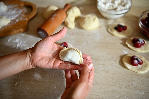 high angle view of a raw dumpling on female chef pastry hands on the background of kitchen countertop - Вареники с вишней