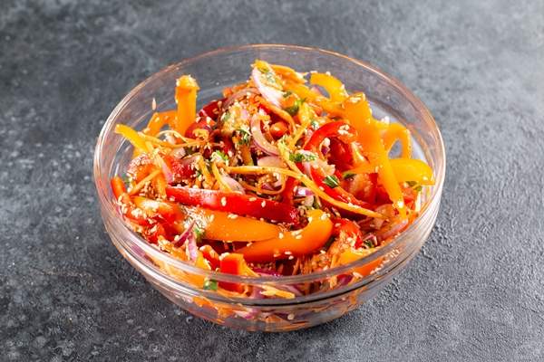 sweet peppers with korean carrots sesame seeds and vegetables in a bowl on a dark background spicy healthy food - Острый салат из болгарского перца с морковью и кунжутом
