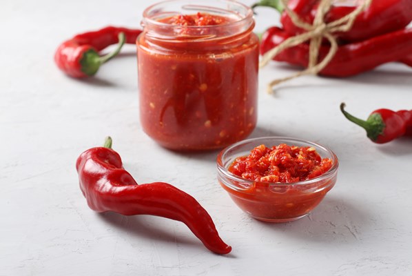 traditional sauce adjika with hot chili pepper paste harissa on light background - Закуска овощная "Огонёк"