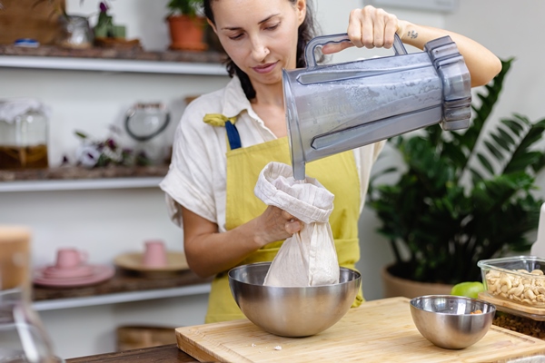 woman squeezing almond milk from almond in kitchen at home - Миндальное молоко