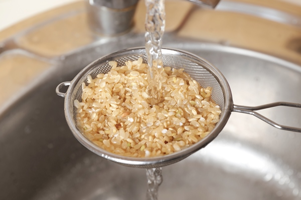 washing raw brown rice in colander over kitchen sink - Плов с сухофруктами и каштанами