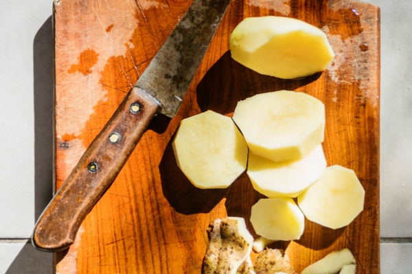 high angle view of sliced potatoes with knife on wooden cutting board - Картофель с огурцами в горшочке
