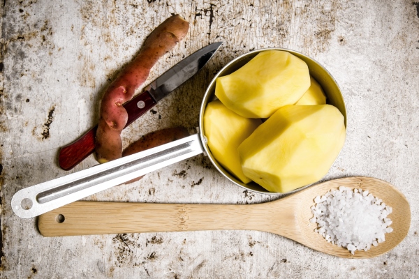 the peeled potatoes in a metal saucepan with a spoonful of salt on the rustic - Цеппелины с грибной начинкой, постный стол