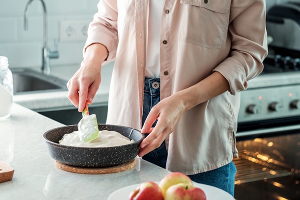 a woman in the kitchen is leveling the dough for making a pie with apples with a spatula in a baking dish cooking baking from rice flour - Пирог "Мечта" с яблоками