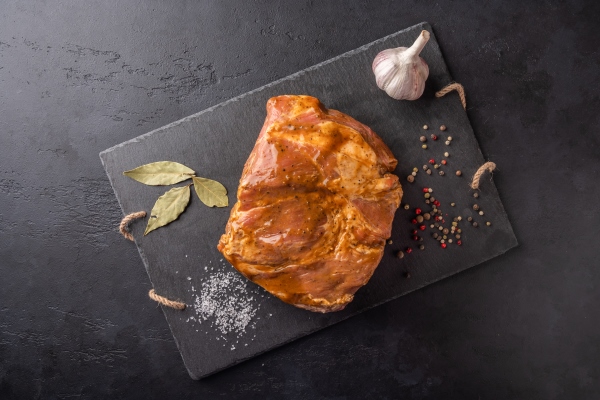 ingredients for cooking homemade baked meat in marinade on a marble board on a dark background - Буженина домашняя