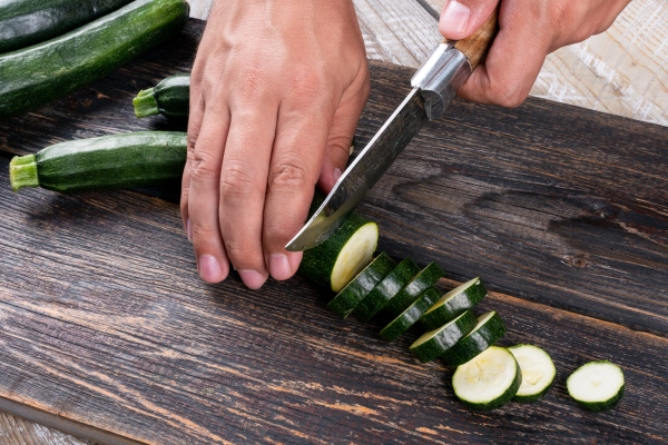 man cutting fresh zucchinis into slices on a cutting board on a wooden table - Чесночный суп-пюре