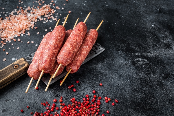 raw lula or kofta kebabs skewers on a butcher cleaver with salt and pepper black background top view copy space - Люля-кебаб