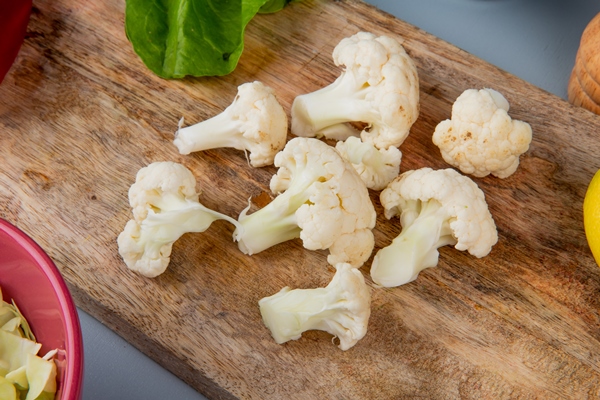 close up view of cauliflower pieces with spinach on cutting board and cabbage slices on blue background - Овощной суп с сыром для детей до 1 года