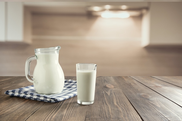 glass of fresh milk and jug on wooden tabletop with blur kitchen as background - Овощной суп с сыром для детей до 1 года