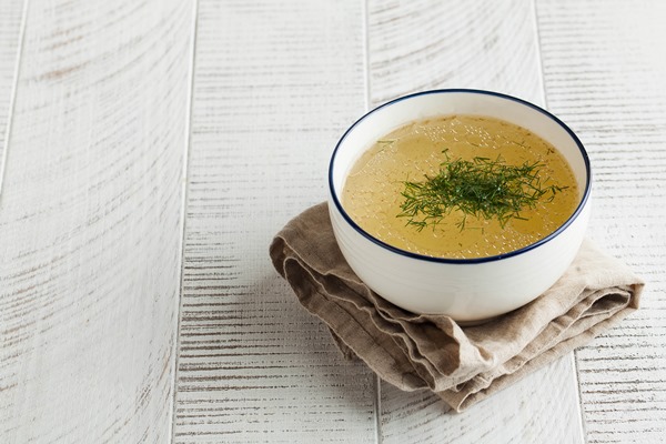 homemade bone broth in a white bowl on a wooden table the concept of healthy eating copy space - Пюре из курицы и риса с морковью и яблоком (питание детей до 1 года)