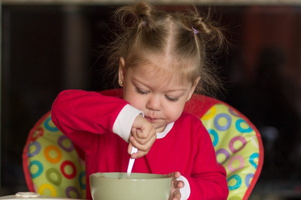 portrait of little girl eating porridge using spoon sitting in feeding chair - Печёночные котлеты (для детей 1-2 лет)