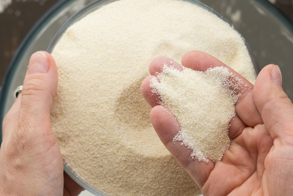 top view of womah hand putting semolina into bowl with milk as ingredient for baking mannik casserole on the brown background - Печёночные оладьи