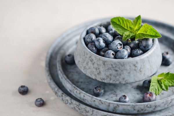 ripe sweet blueberries in blue bowl on a gray concrete - Постный смузи-боул с бананом, киви, клубникой, голубикой