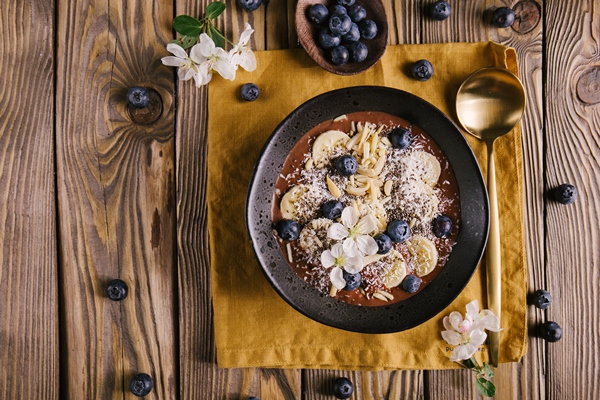 smoothie bowl on white plate on wooden table - Постный смузи-боул с финиками и орехами