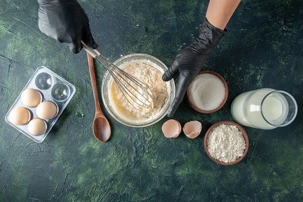 top view female cook mixing up flour in plate with eggs on a dark surface - Венские вафли в духовке