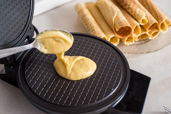 waffle iron in the kitchen preparing homemade waffles pouring a dough - Вафельные трубочки
