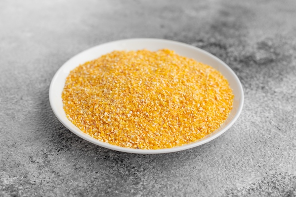cornmeal mush in a white saucer on a gray concrete background - Драники постные с кукурузной крупой