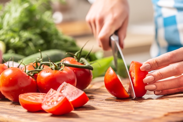 detail of a tomato freshly cut into halves on a cutting board with cucumber garlic and more tomatoes aside - Овощной салат с киноа