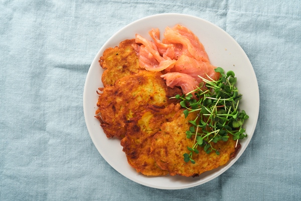 potato pancakes fried homemade potato pancakes or latkes with cream green onions microgreens red salmon and sauce in rustic plate on blue linen tablecloth rustic style healthy food top view - Драники постные с кукурузной крупой