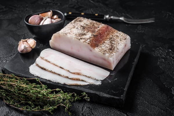 sliced salty lard with garlic and black pepper on marble board black background top view - Консервирование пищевых продуктов