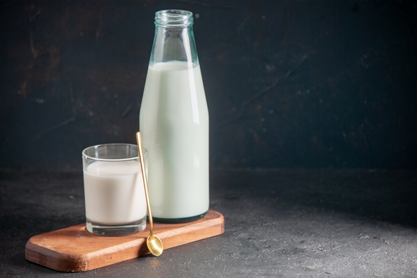 top view of delicious milk in glass and bottle golden spoon on wooden tray on the right side on dark surface - Диетическая творожная пасха
