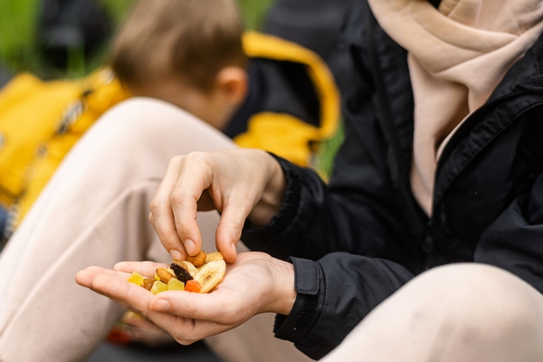 a woman holds various dried fruits and nuts in her hand sits on the green grass in the forest snack during the hike walk healthy vegetarian food - Организация трапезы в походе: хранение продуктов, походная кухня, утварь, меню