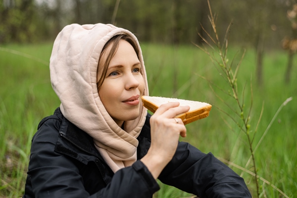 an adult attractive woman eats a sandwich outdoors in the forest park snack on a hike on a walk - Питание в походе