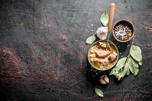 canned meat in a tin with garlic spices and bay leaf on dark wooden table - Фронтовой гороховый суп