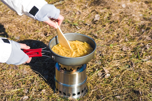 close up hands of woman hiker cooking pasta on wood burner in wild camping - Организация трапезы в походе: хранение продуктов, походная кухня, утварь, меню