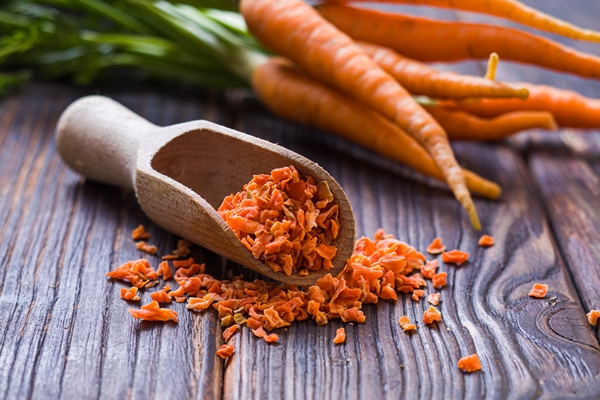 closeup dried and ground carrot seasoning with bunch of fresh carrots behind small wooden scoop filled with bright orange carrot condimet wooden surface - Морковный чай с чагой