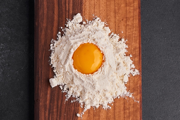egg and flour mixed with each other on wooden board on black surface - Котлеты из риса и консервов